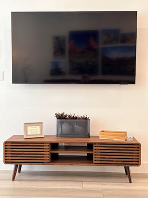 A modern entertainment center with a flat-screen TV mounted on the wall, a framed welcome sign, a potted plant, and a wooden box on the console. - The Desert Belle, No. 1 Loft at The Lofts,  4BR 3.5BA Southern Utah Retreat (Saint George)