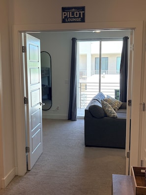 A room with a bed, a window with curtains, a door, and a sign that reads 'PILOT LOUNGE'.