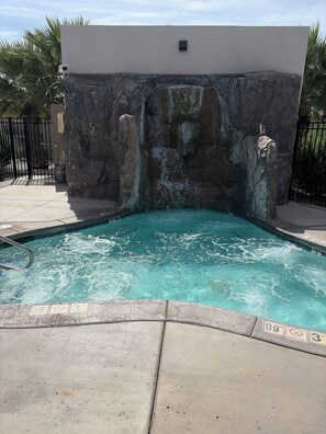 A swimming pool with a waterfall feature, surrounded by a stone wall and a metal fence. - The Desert Belle, No. 1 Loft at The Lofts,  4BR 3.5BA Southern Utah Retreat (Saint George)