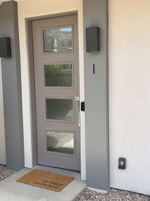 A grey door with three glass panels, a doormat with a welcoming message, and a wall-mounted intercom. - The Desert Belle, No. 1 Loft at The Lofts,  4BR 3.5BA Southern Utah Retreat (Saint George)