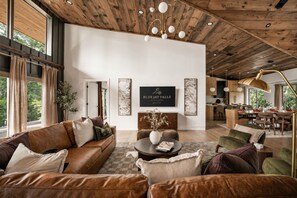 A spacious living area with a high ceiling and wooden beams, a dining area, and a kitchen. - Blue Jay Falls Overlook: Luxury Cabin, Hot Tub, Sauna, Game Room & Views (Ellijay)