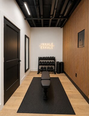 Une salle de sport équipée d’un banc, d’haltères et d’un néon sur lequel on peut lire : « INSPIRER, EXPIRER ».
