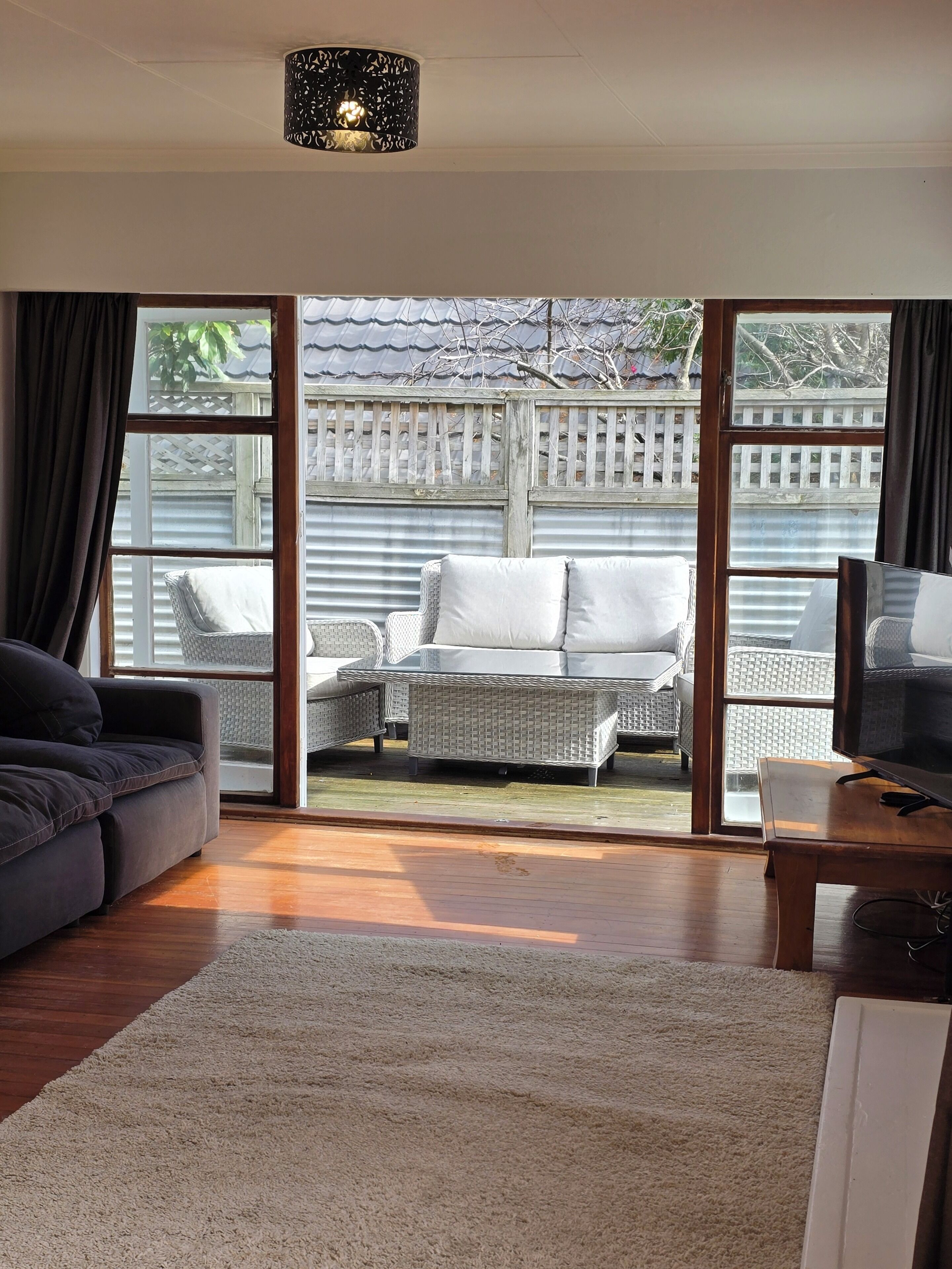 A living room with a sofa, a TV, and a large window with a view of a fenced outdoor area.