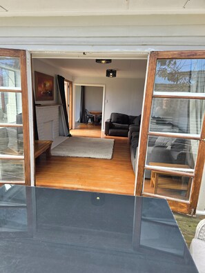 An open living space with a sofa, a fireplace, a dining table, and a view through a window. - Middleton Near The Beach (Paraparaumu Beach)