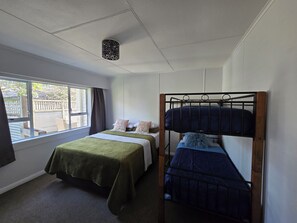 A room with a bunk bed, a single bed, a window with a view of the outside, and a ceiling light fixture.