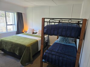 A room with bunk beds, a window with curtains, and a bedside table with a lamp. - Middleton Near The Beach (Paraparaumu Beach)