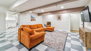 A spacious living room with a large orange sofa, a patterned rug, and a flat-screen TV on a wooden cabinet.