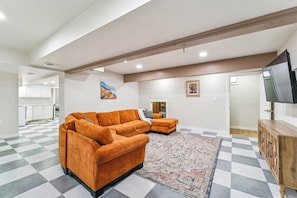 A spacious living room with a large orange sofa, a patterned rug, and a flat-screen TV on a wooden cabinet.