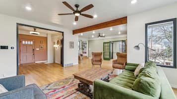 Un salon spacieux avec un canapé vert, une table basse en bois et un ventilateur de plafond.