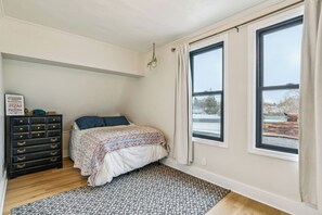 Et soveværelse med seng, kommode, vinduer og udsigt til det fri.