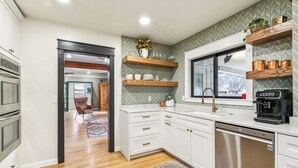 A modern kitchen with white cabinetry, a dishwasher, a coffee maker, and a window with a view.