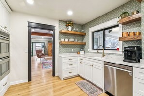A modern kitchen with white cabinetry, a dishwasher, a coffee maker, and a window with a view.