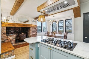 Una cocina con chimenea de ladrillo, una isla grande con estufa a gas y un comedor con mesa y sillas.