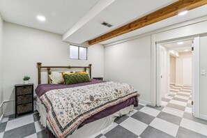 A bedroom with a checkered floor, a bed with a floral bedspread, a wooden headboard, and a small bedside table with a plant.