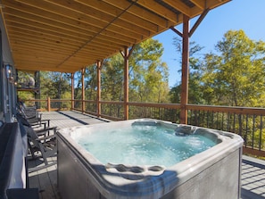 A hot tub on a wooden deck with a wooden railing and chairs. - NEW Luxe 12BR Cabin w/Indoor Pool & Movie Theater (Sevierville)