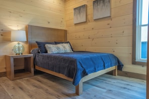 A wooden-paneled bedroom with a bed, a nightstand, and a window. - NEW Luxe 12BR Cabin w/Indoor Pool & Movie Theater (Sevierville)