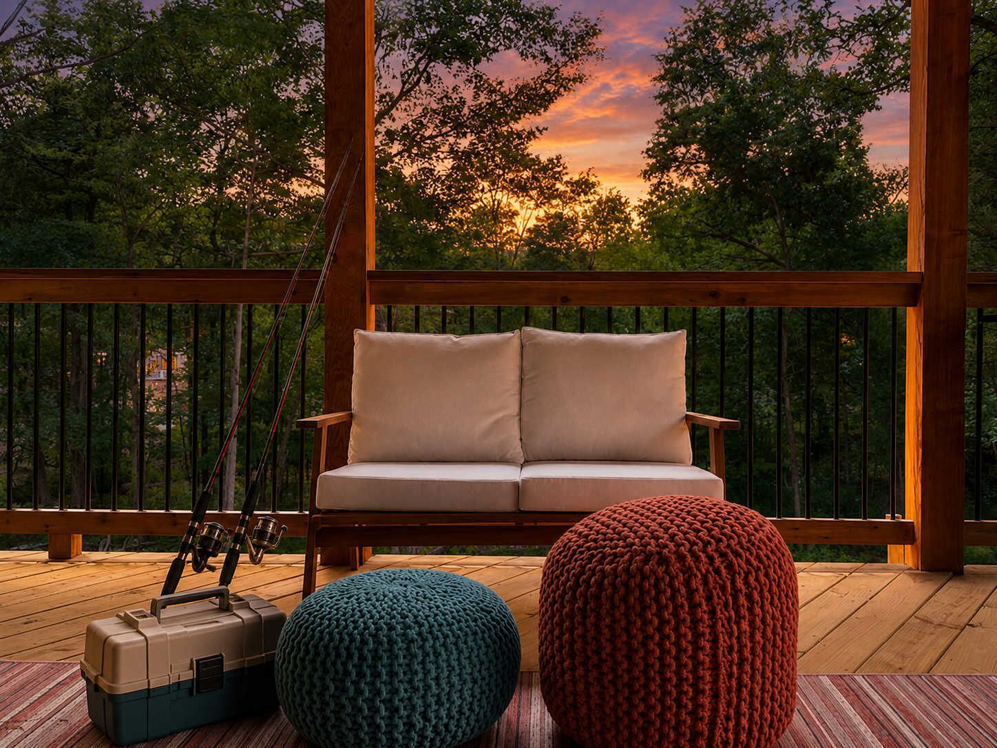 A wooden deck with a sofa and two knitted poufs, a fishing rod, and a cooler.