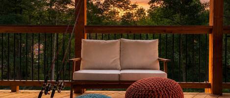 A wooden deck with a sofa and two knitted poufs, a fishing rod, and a cooler.