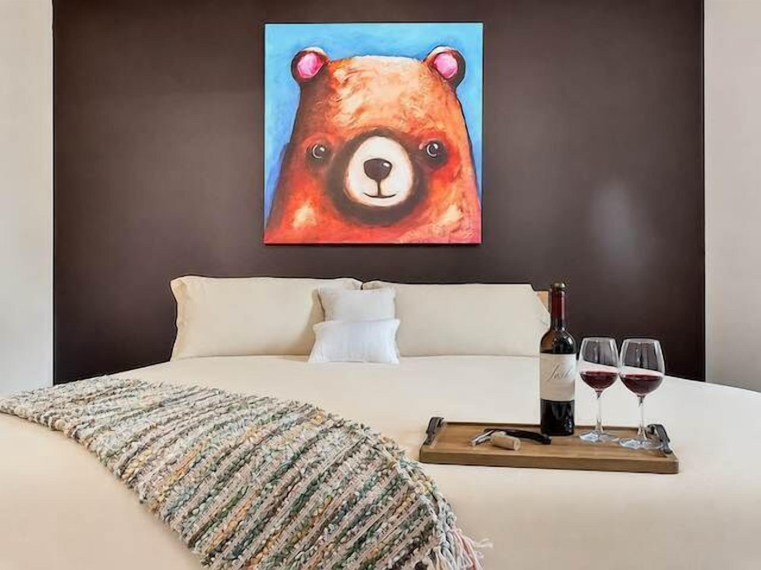 Ein Bett mit einem Bärenbild, einer Flasche und zwei Gläsern auf einem Tablett.