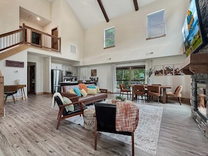 A spacious living area with a high ceiling, a dining table, and a fireplace.