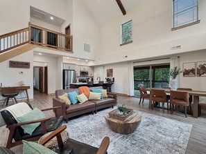 A spacious living area with a high ceiling, a staircase, a kitchen, and a dining area. - Luxury 4BR Cabin | Lazy River | Near Big Cedar (Hollister)