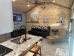 A modern kitchen with a granite countertop, a black sofa with a cowhide throw, and a dining area with a wooden table and chairs.
