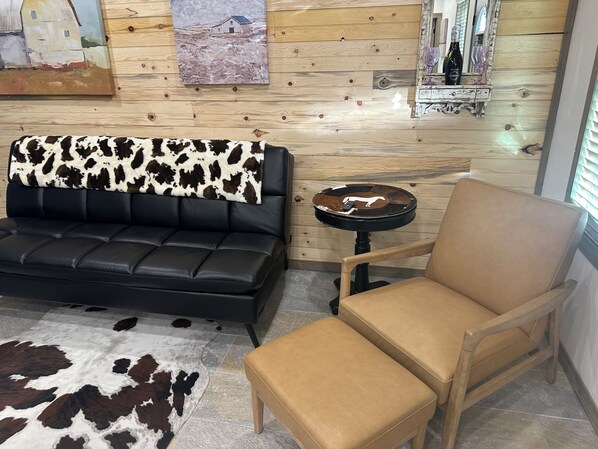 A living room with a black leather sofa, a tan armchair, a small round table, and a cowhide rug.