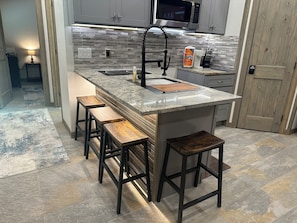 A kitchen with a central island, bar stools, a microwave, and a soap dispenser.