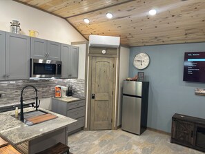 Une cuisine moderne avec des meubles gris, un réfrigérateur en acier inoxydable, un four à micro-ondes et une horloge murale.