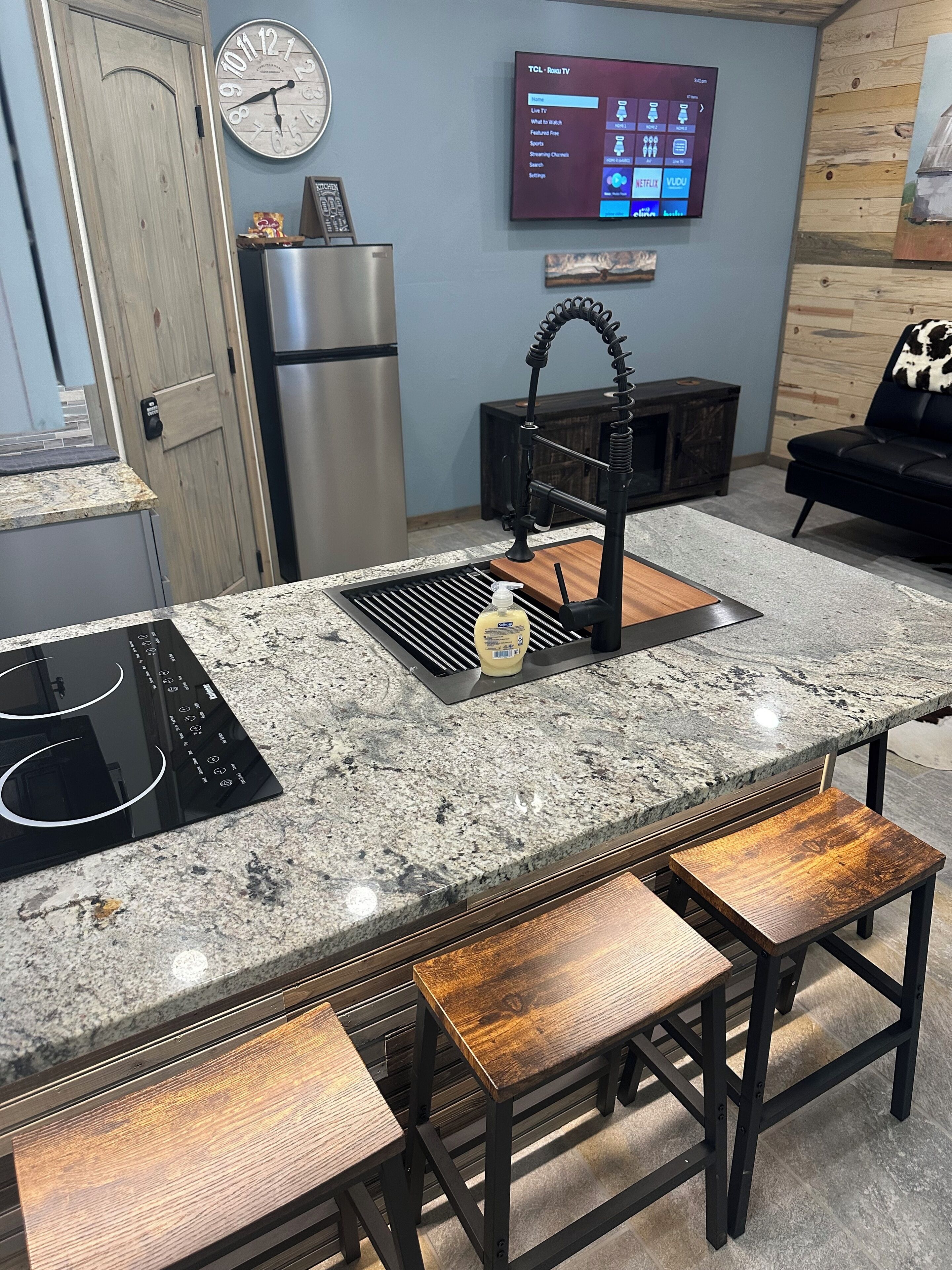 A modern kitchen with a granite countertop, stainless steel appliances, a built-in oven, and a wooden bench.