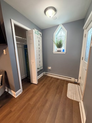 A hallway with a wooden floor, a white door, a window with a plant, and a wall-mounted sign.