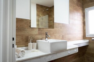 Un baño con lavamanos blanco, un espejo y zona de ducha.