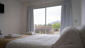 A hotel room with a large bed, a view of the outdoors, and a window with curtains. - Hotel Cantera Respira Campo (Las Chacras)