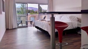 A modern hotel room with a bed, a red bar stool, and a view of the outdoors. - Hotel Cantera Respira Campo (Las Chacras)