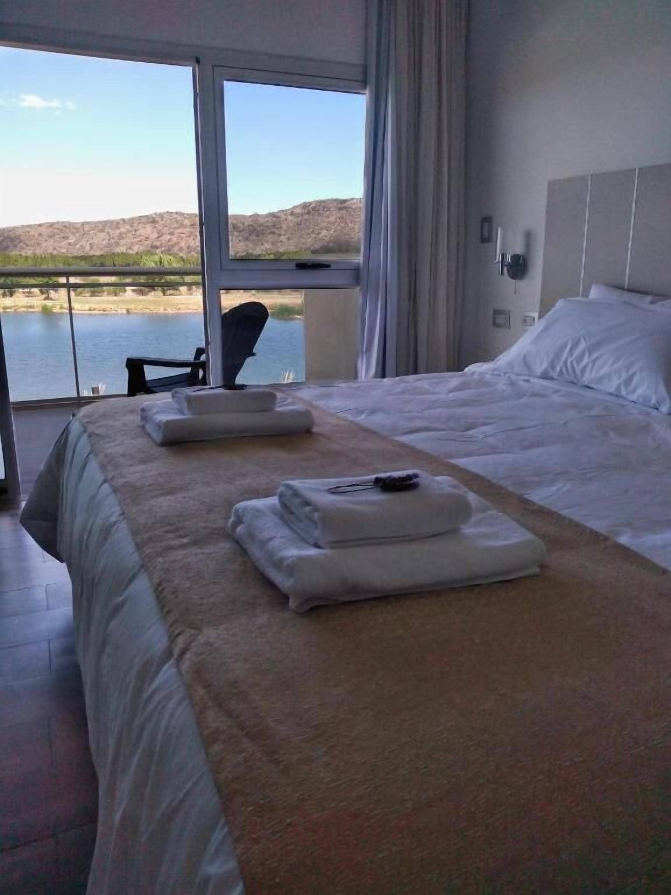 A hotel room with a large bed, a view of a lake, and a chair by the window.
