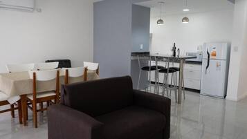 Una sala de estar moderna con sofá, mesa de comedor, sillas y una cocina con refrigerador, estufa y taburetes de bar.