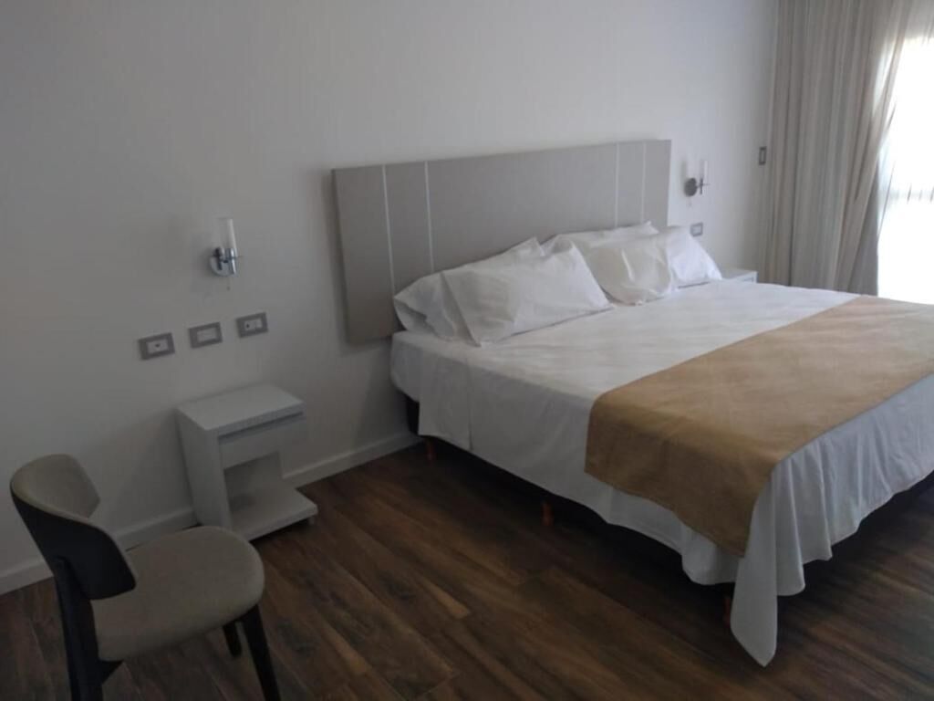 Habitación de hotel con cama, mesita de noche, silla y escritorio pequeño.
