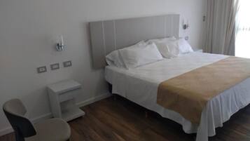 Habitación de hotel con cama, mesita de noche, silla y escritorio pequeño.