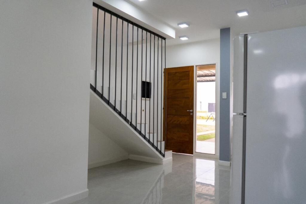 Un pasillo con una escalera, una puerta y un refrigerador.