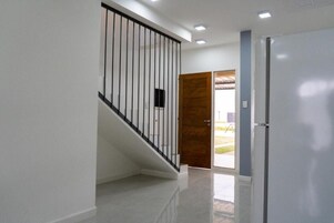 Un pasillo con una escalera, una puerta y un refrigerador.