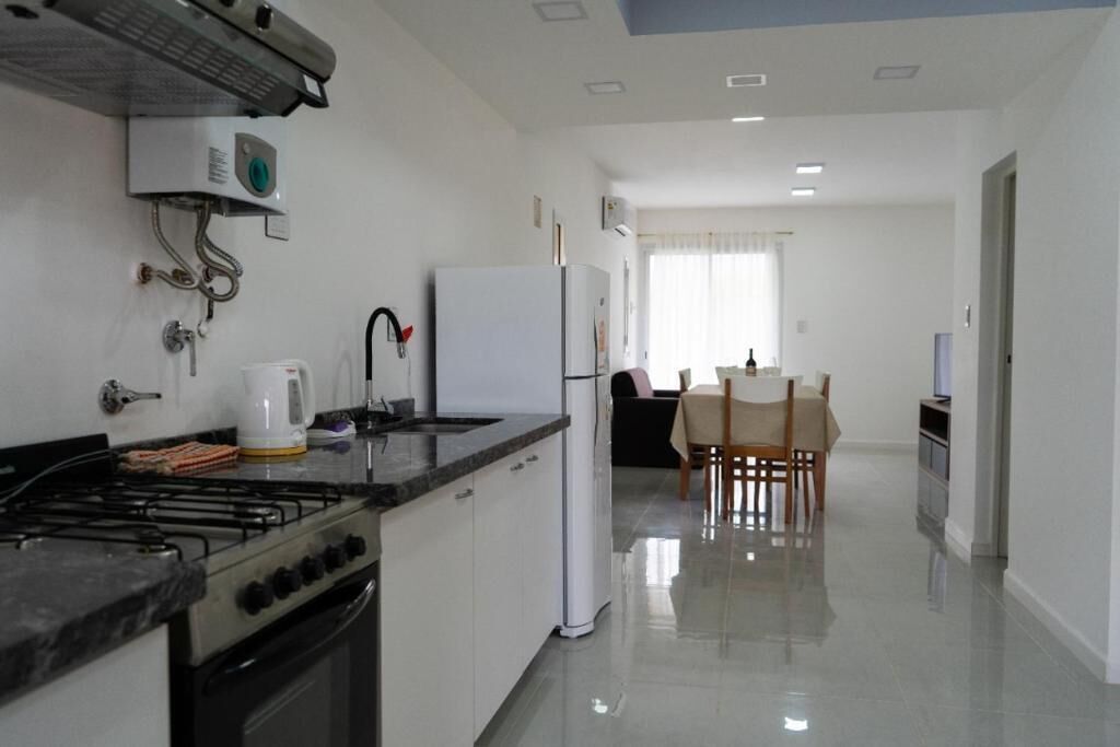 A modern kitchen with a gas stove, white cabinets, a refrigerator, and a dining area with a table and chairs.