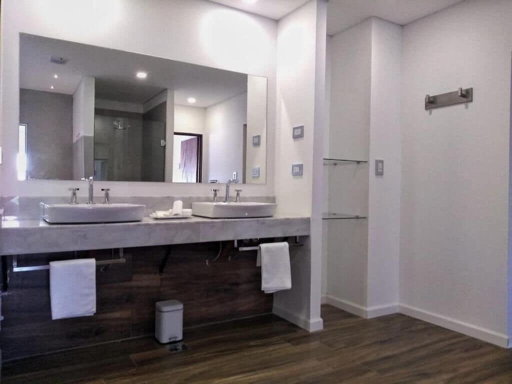 A modern bathroom with two sinks, a large mirror, and a shower area.
