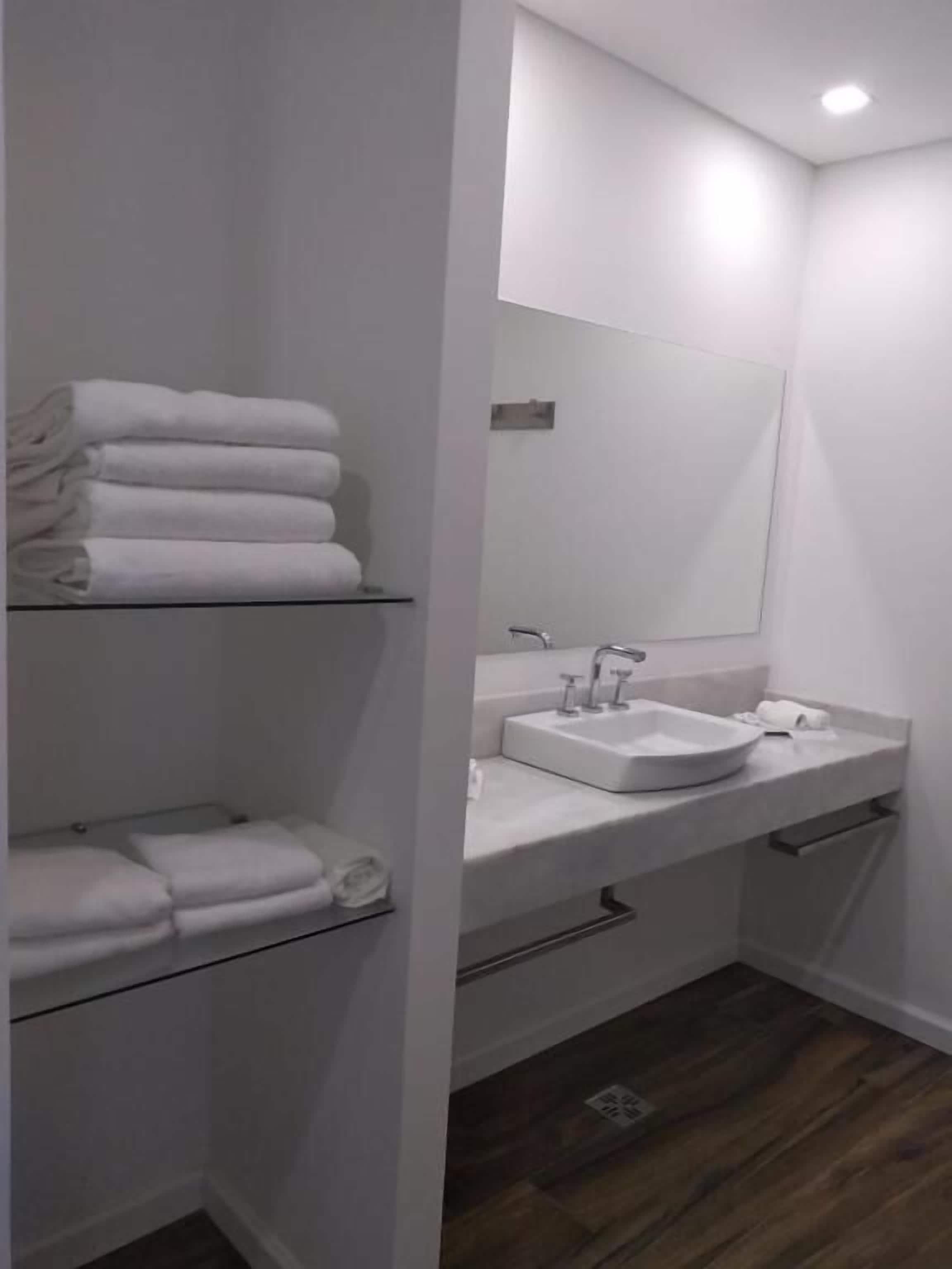 A modern bathroom with a white sink, mirror, and shelves for towels.