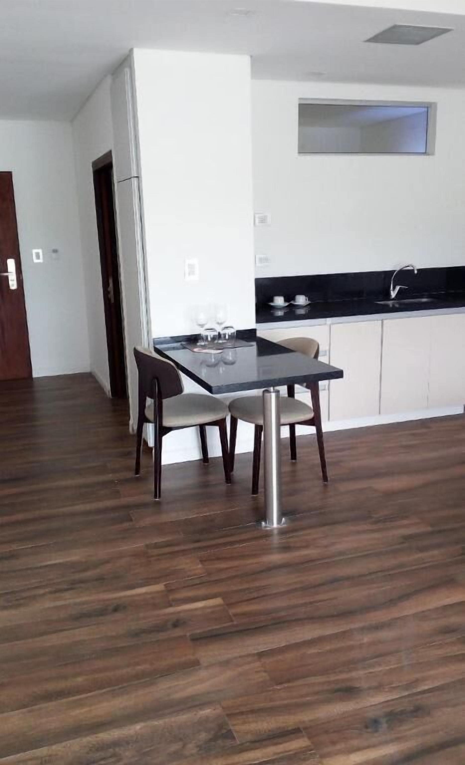 A modern kitchen with a black countertop and white cabinets, a dining area with a table and chairs, and a wooden floor.