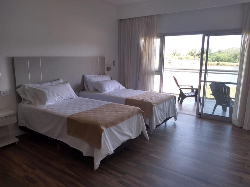 Habitación de hotel con dos camas, un balcón con sillas y vistas al exterior.
