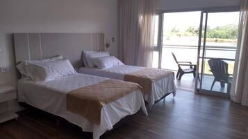 Habitación de hotel con dos camas, un balcón con sillas y vistas al exterior.