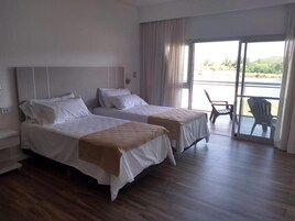 Habitación de hotel con dos camas, un balcón con sillas y vistas al exterior.