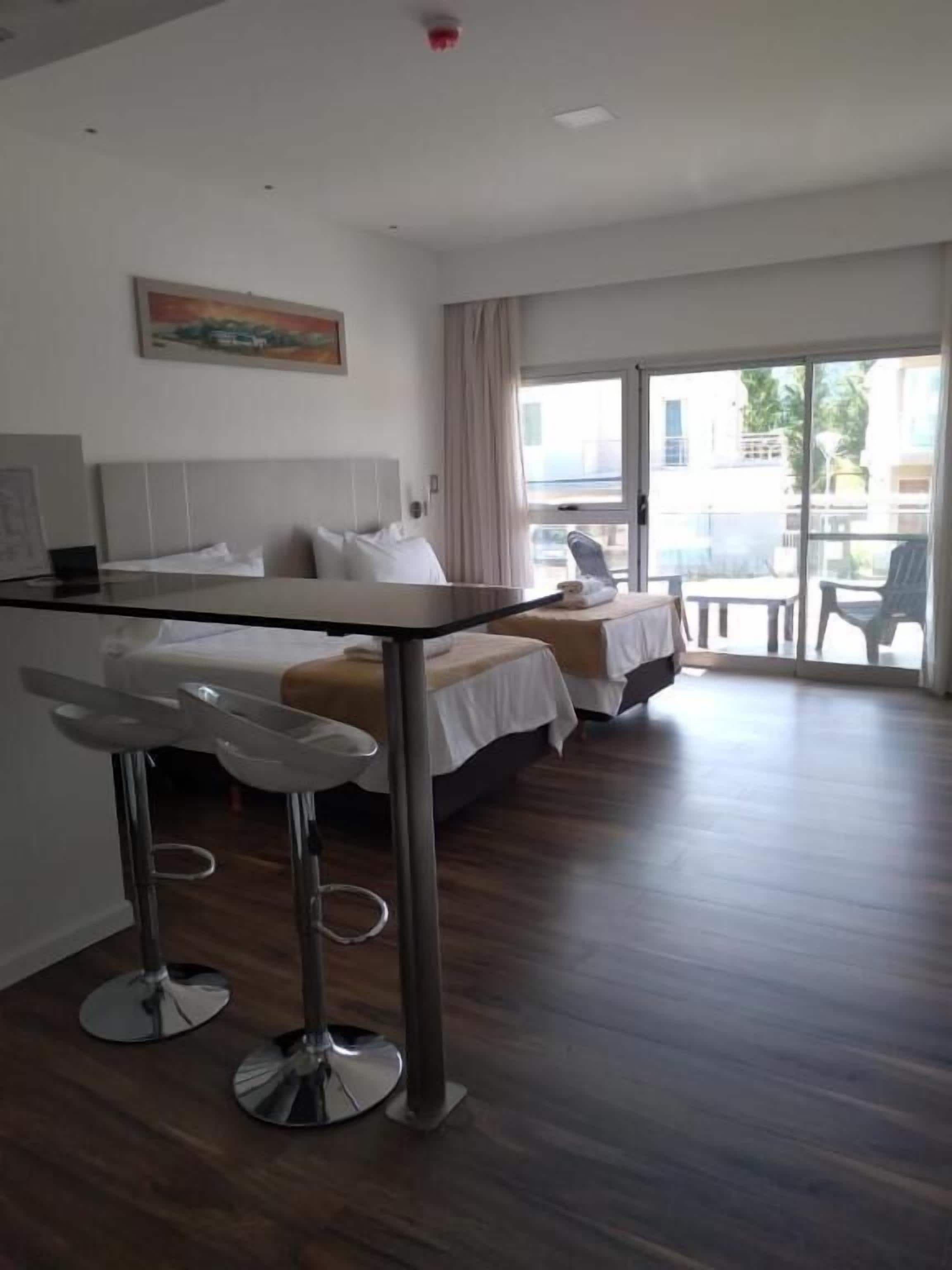 A hotel room with a bed, a desk, and a chair. There is a balcony with a view.