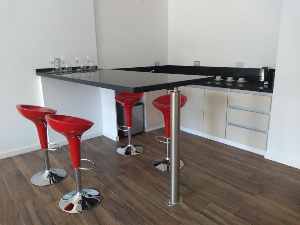 Une cuisine moderne avec un plan de travail noir, des appareils en acier inoxydable et des tabourets de bar rouges.