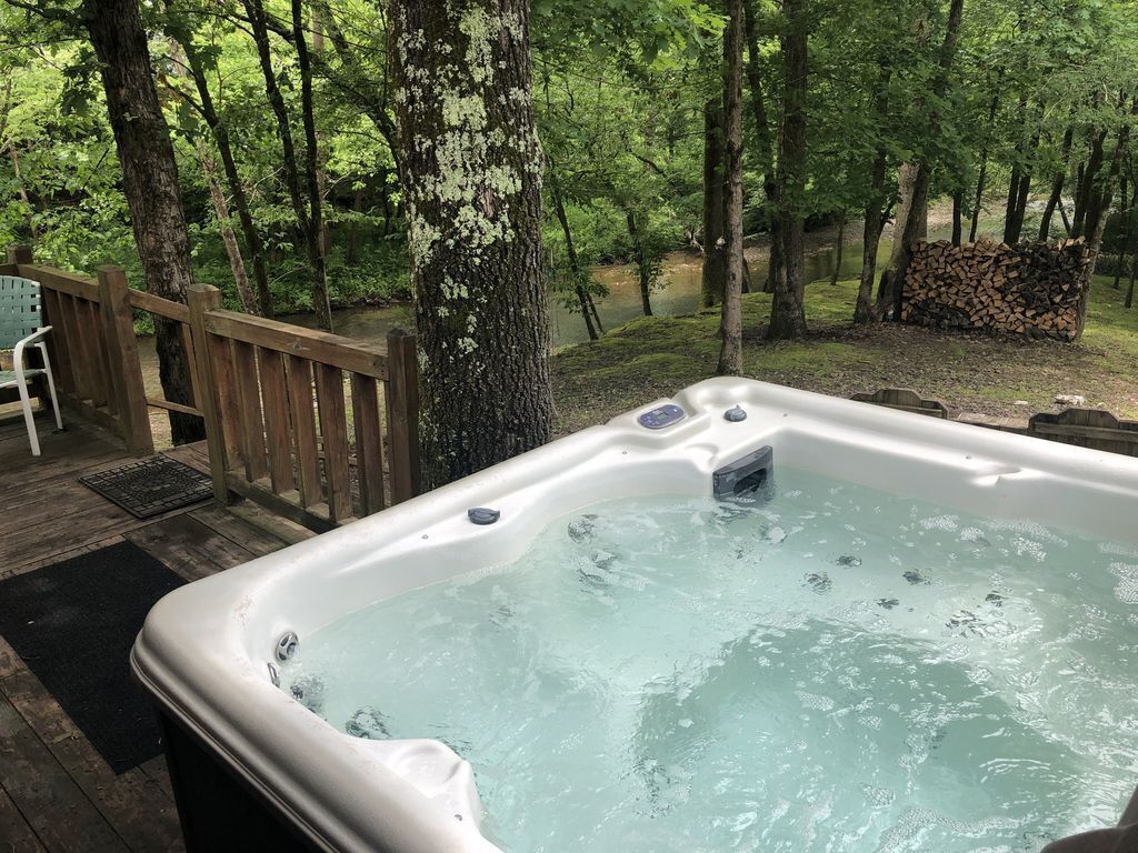 Un bain à remous sur une terrasse en bois, entouré d’arbres.